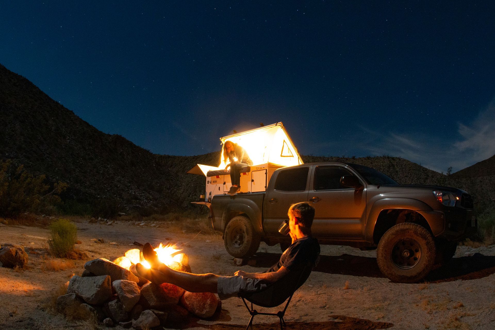 A man is sitting at a campfire in front of a truck.