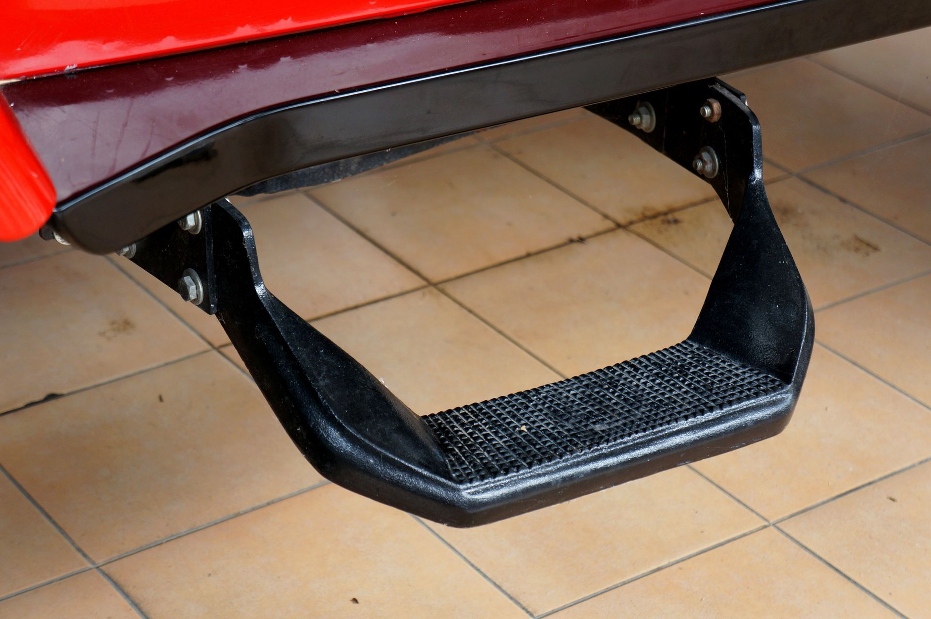 A black step is attached to the back of a red car