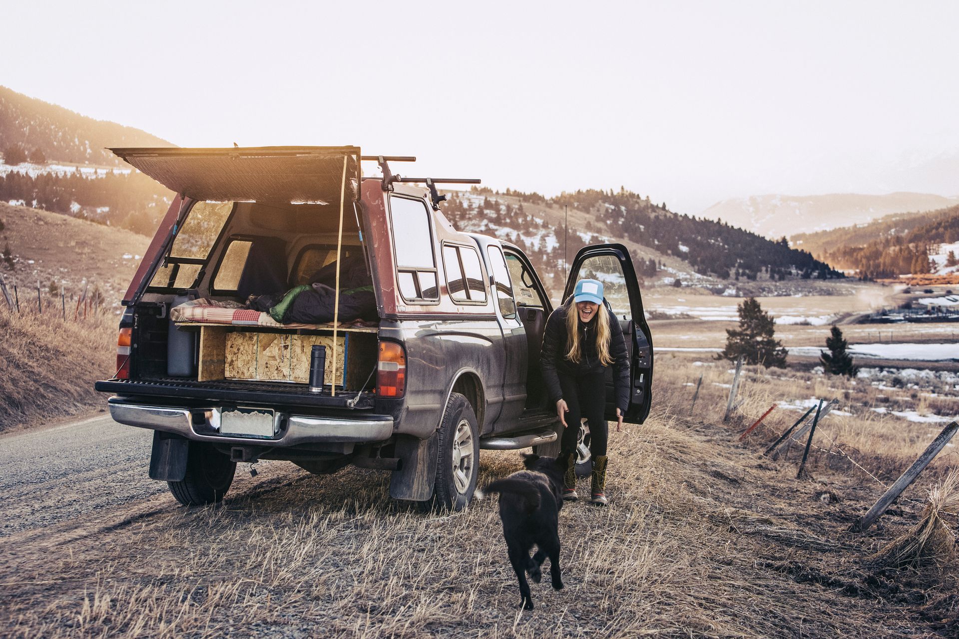 A woman and a dog are standing next to a truck on a dirt road.