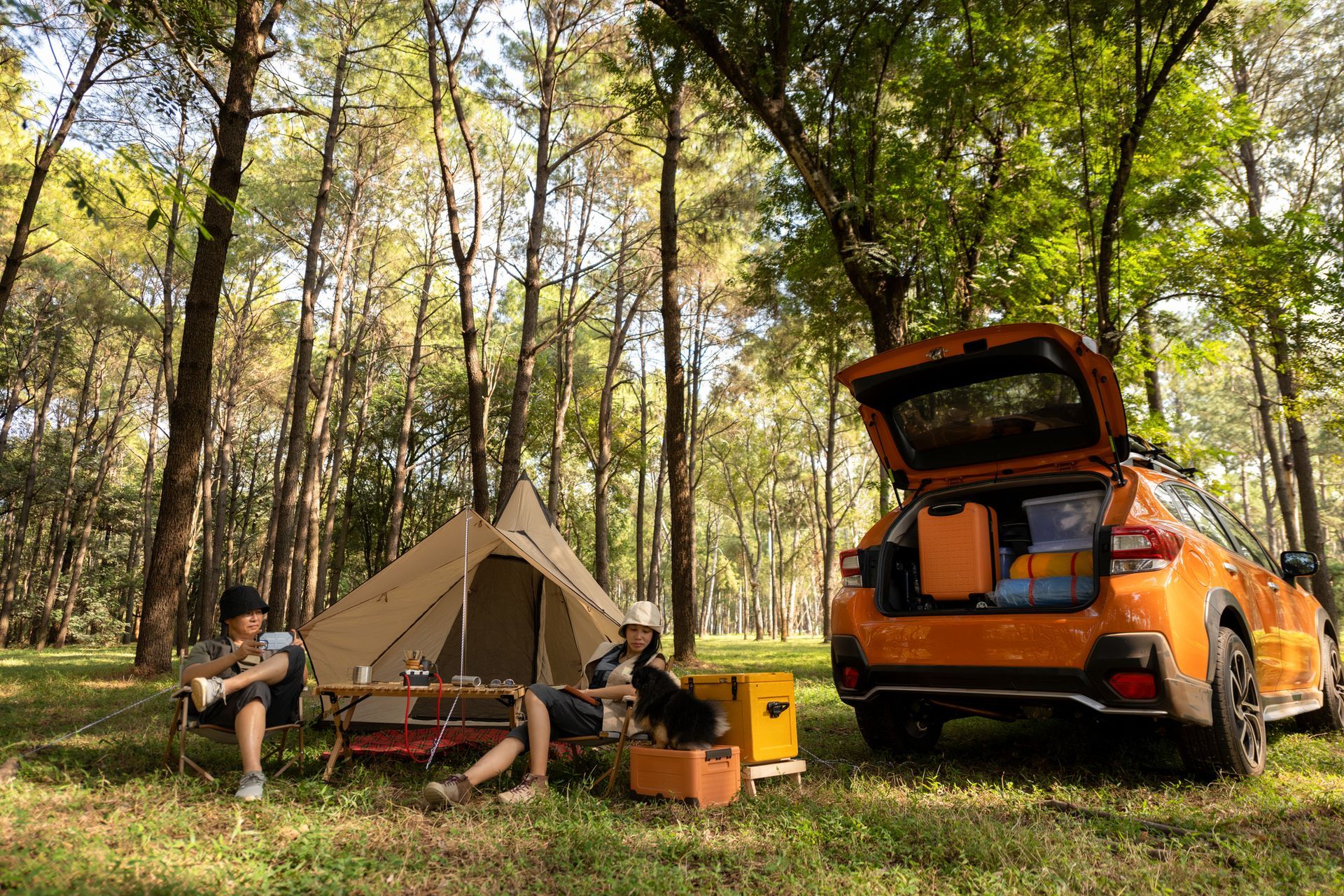 A car is parked in front of a tent in the woods.