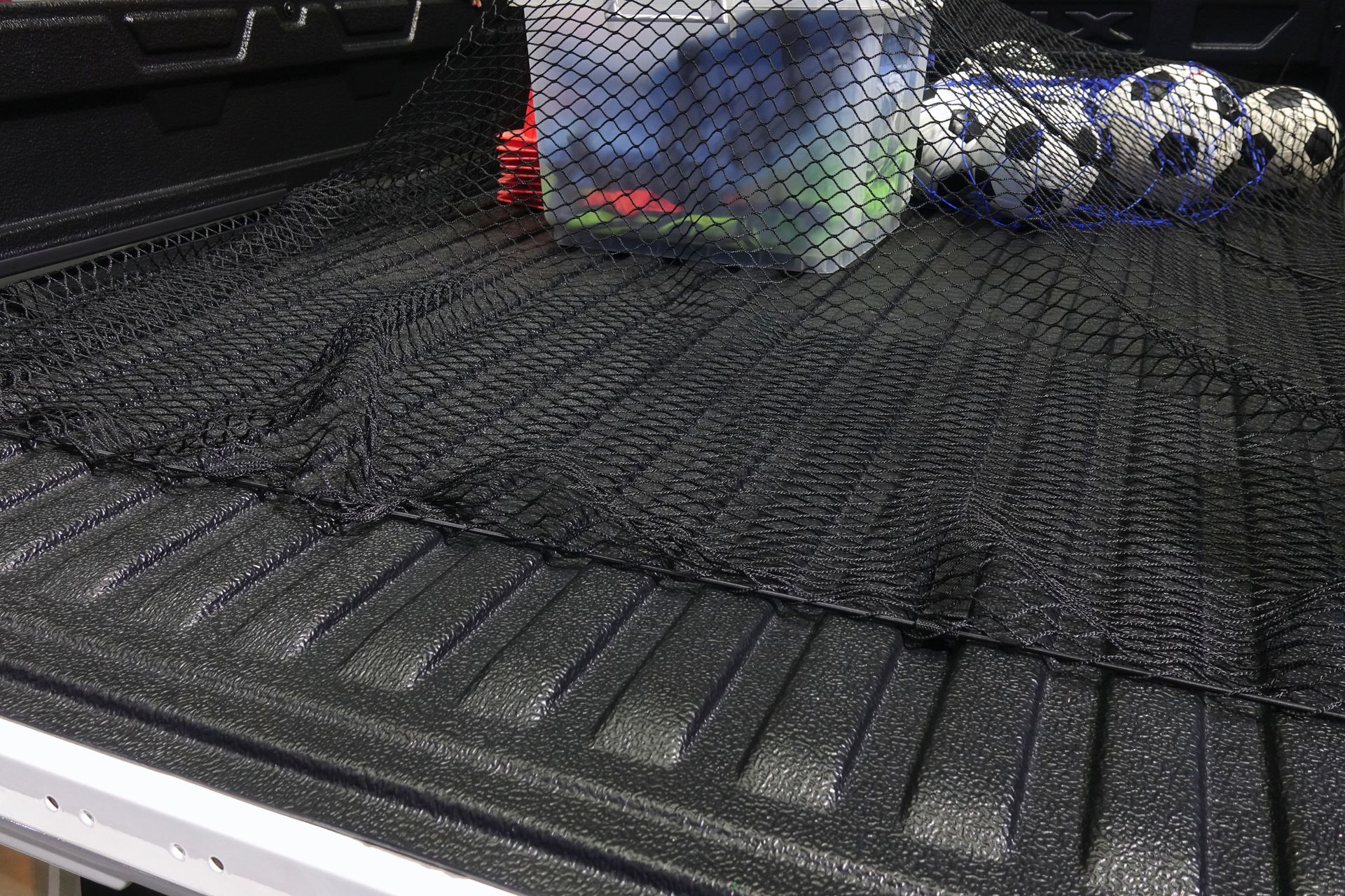 A truck bed with a net and soccer balls in it.