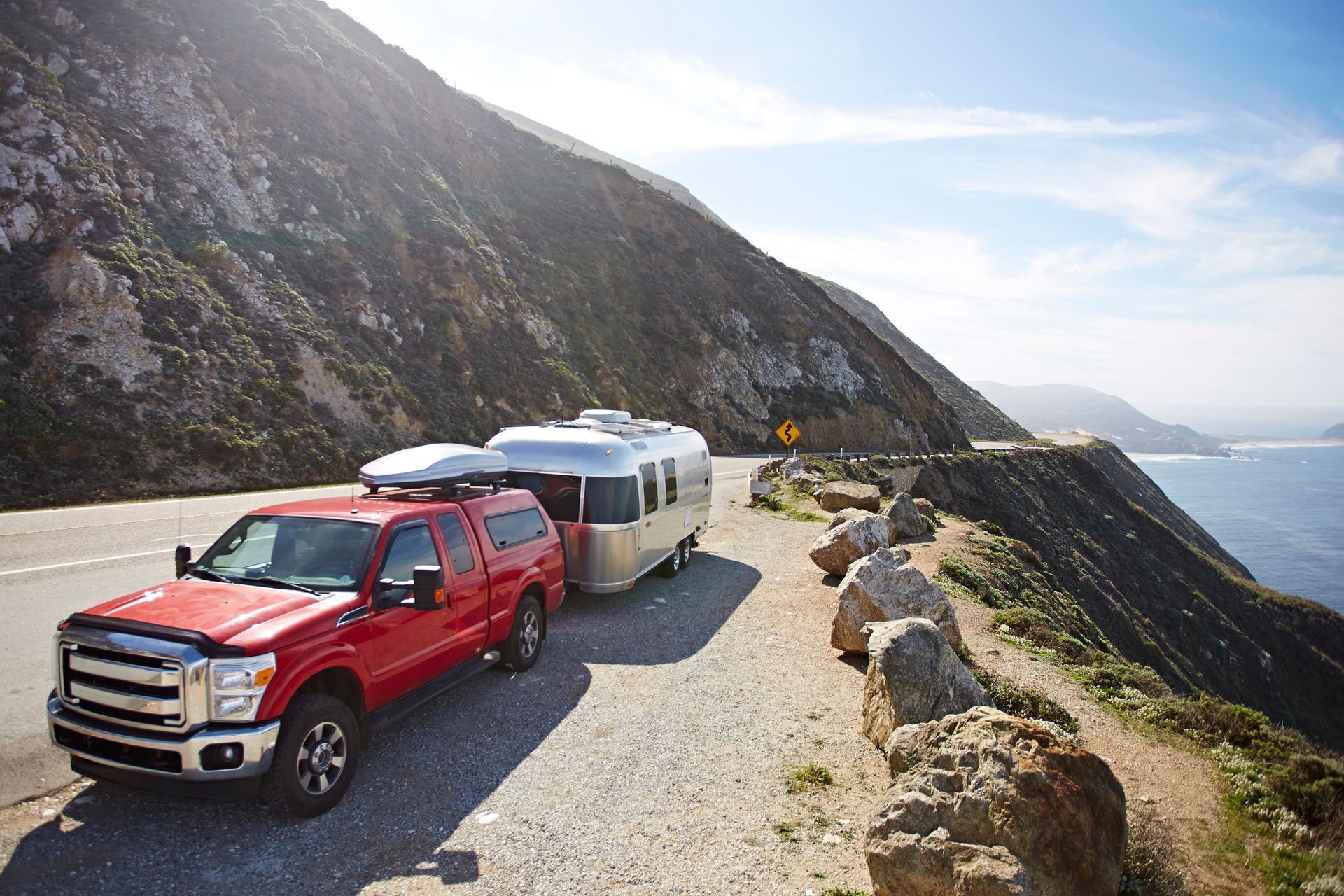 A red truck is towing an airstream trailer down a mountain road