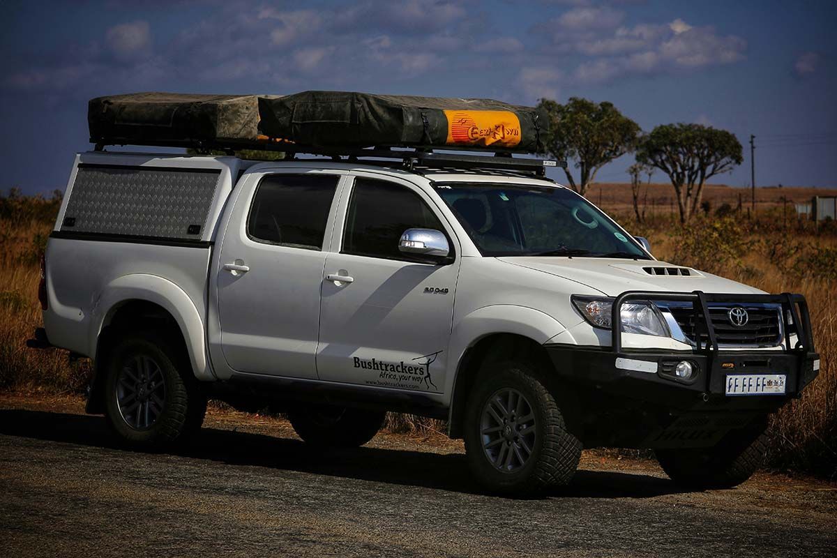 A white truck with a tent on top of it is parked on the side of the road.