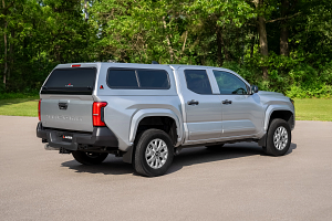 A silver truck with a canopy on top of it is parked on the side of the road.