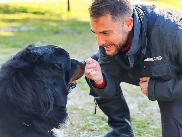 Un hombre acaricia a un perro negro en un parque.