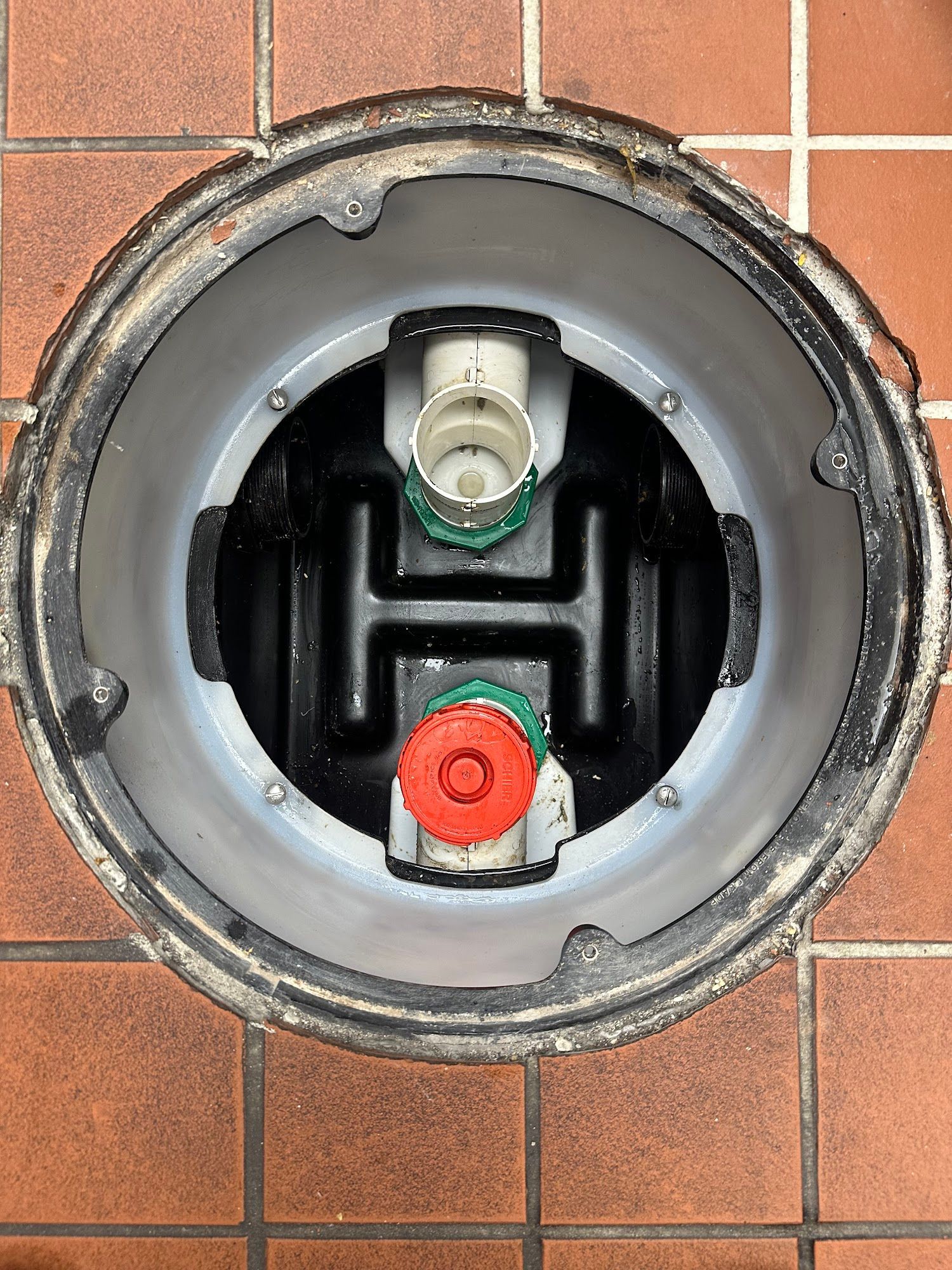 Top-down view of a utility access point. Inside a circular metal frame is a black plastic structure with three colored caps.