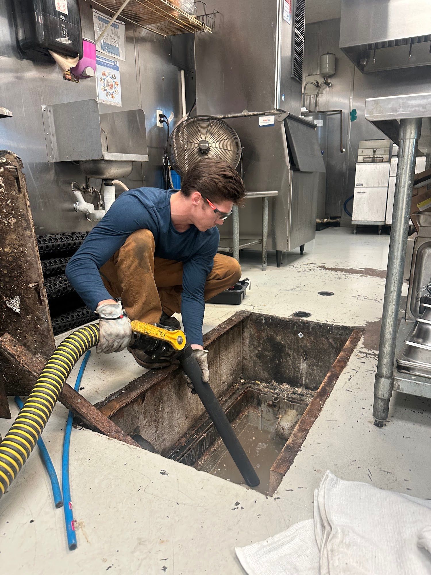 Person uses a vacuum to clean a drain in a commercial kitchen; the drain contains sludge.