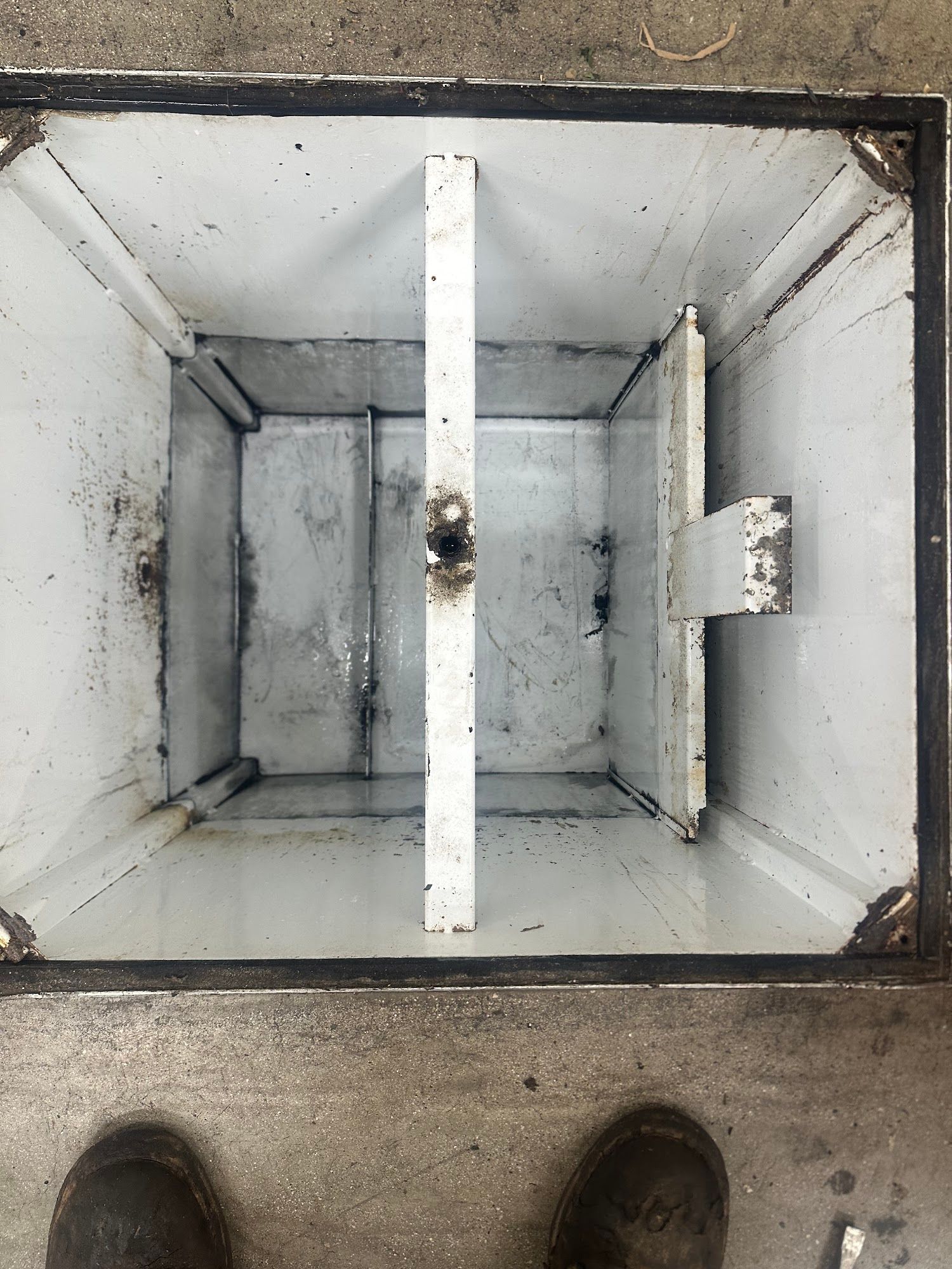 Inside view of a white rectangular metal box with a divider, resting on a concrete surface.
