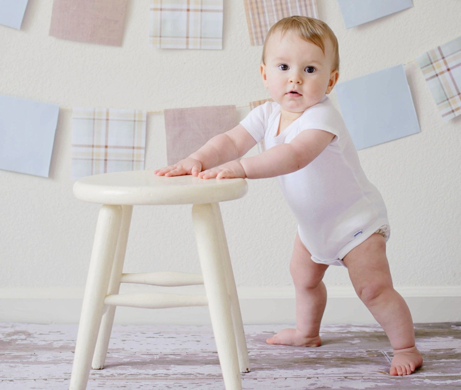 baby standing  with hands on stool  -