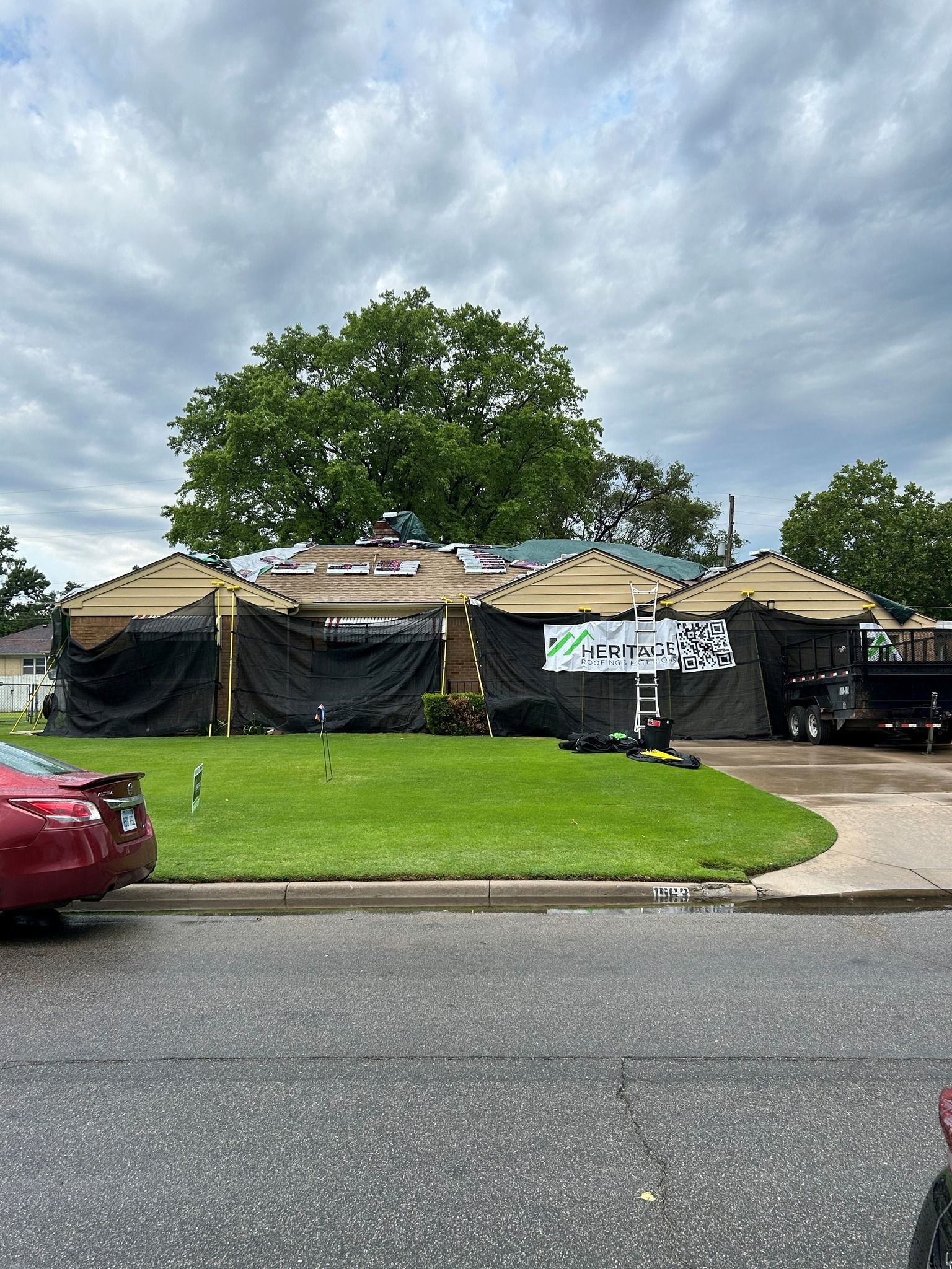 A red car is parked in front of a house that is being remodeled.