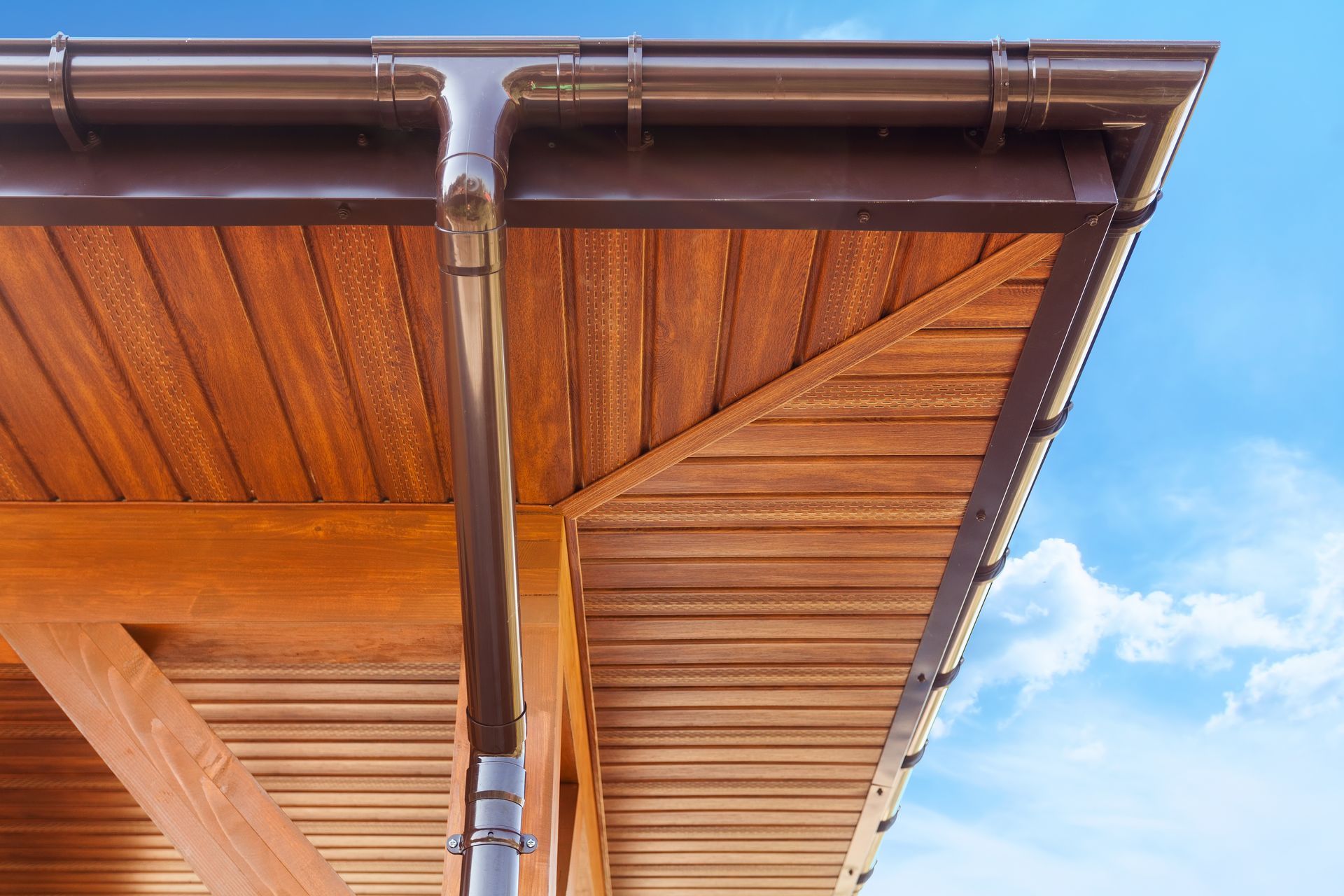 A wooden roof with a brown gutter and a blue sky in the background.