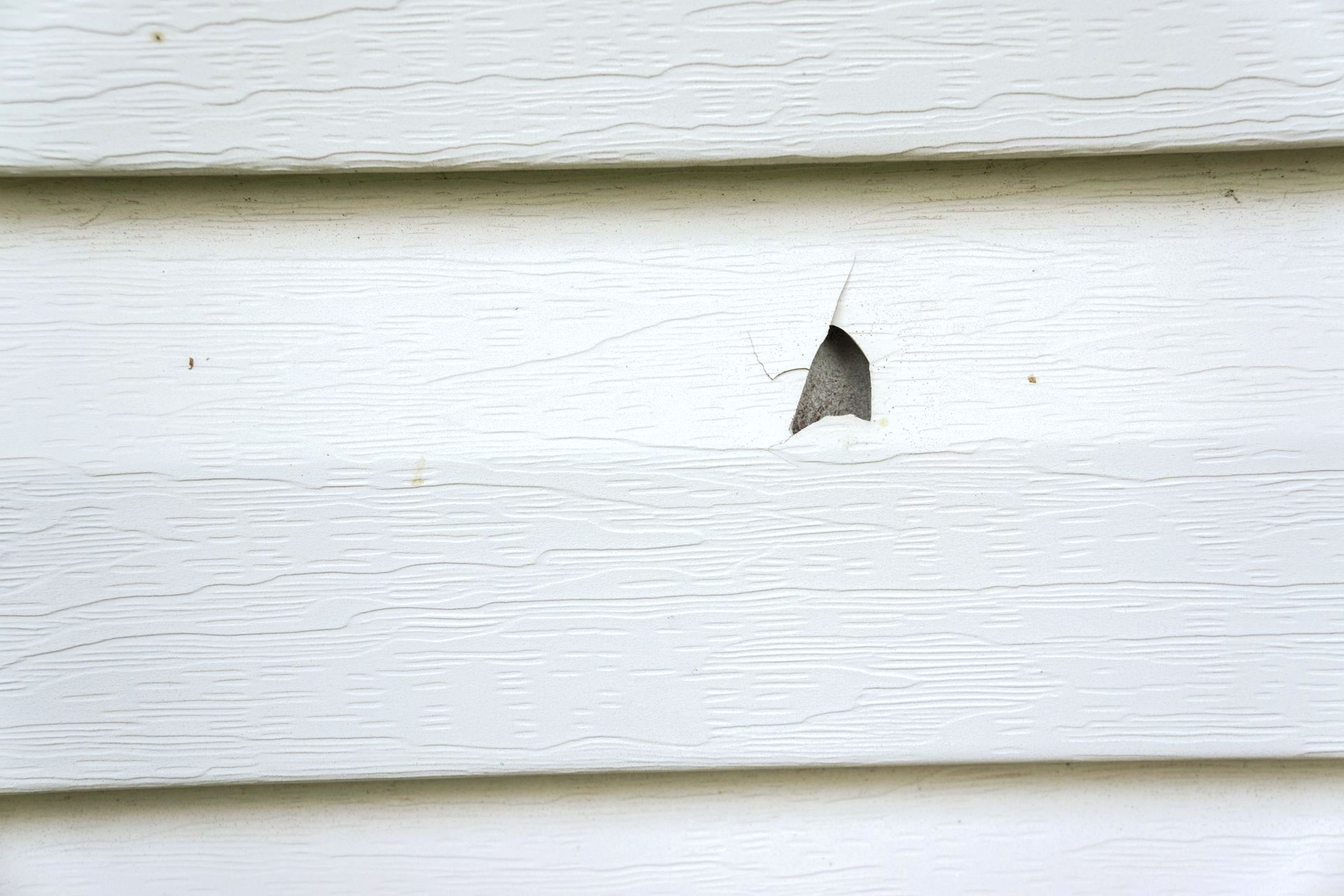 A close up of a white siding with a hole in it.