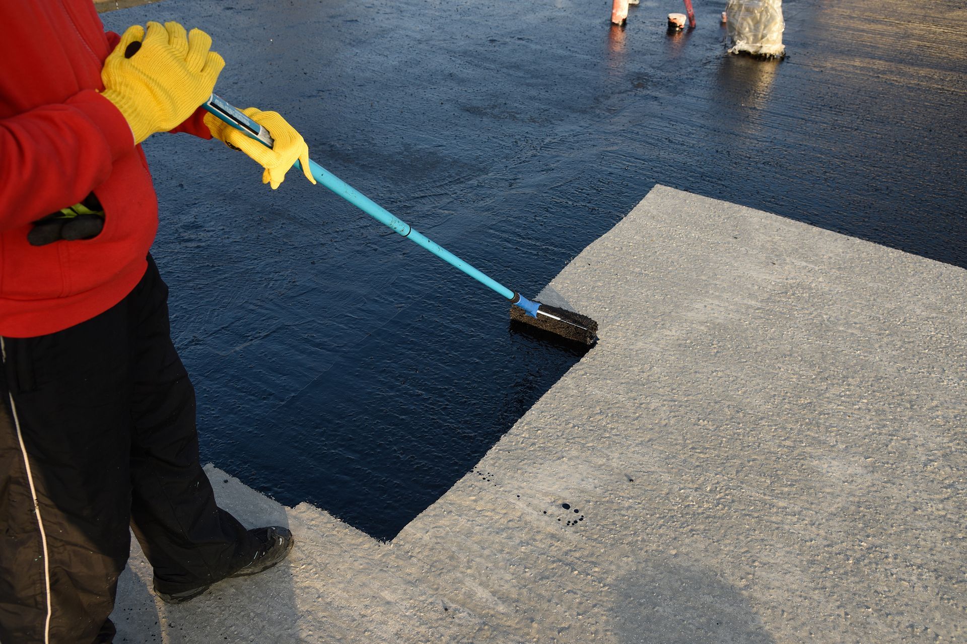 A person wearing yellow gloves is using a broom on a concrete surface.