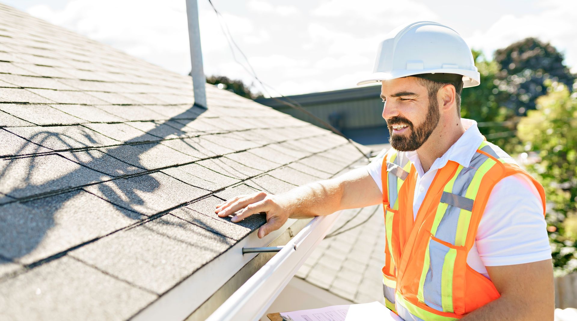 A man wearing a hard hat and safety vest is working on a roof.