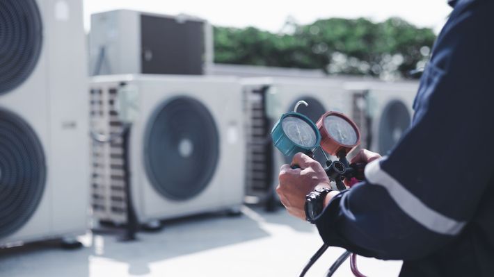 A man is holding a pressure gauge in front of a row of air conditioners.