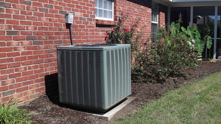 An air conditioner is sitting on the side of a brick house.