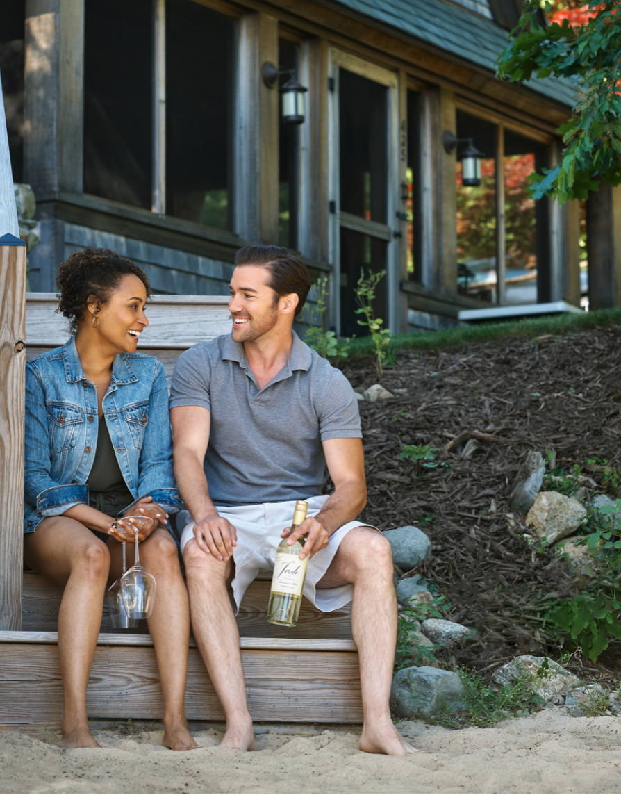 Couple sitting on steps of Sweetheart Village holding wine and wine glasses