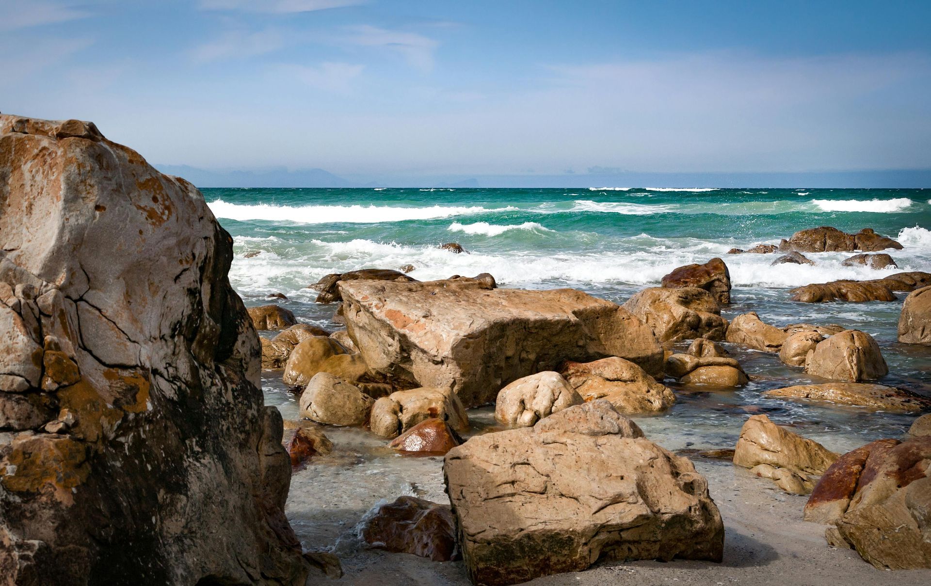 Rocky Cape Cod beach with waves crashing, clear blue sky.