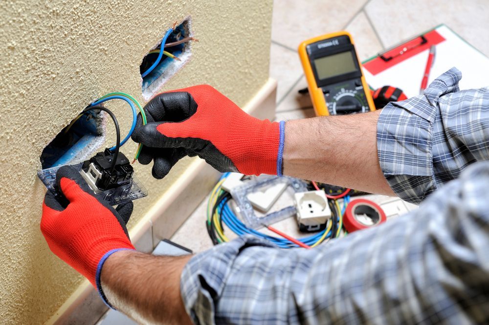 Electrician in red gloves working on an outlet, with tools on a table nearby