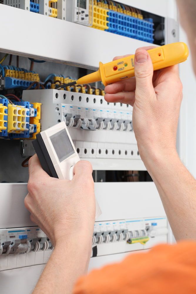 Electrician testing a circuit breaker panel with a voltage tester and multimeter