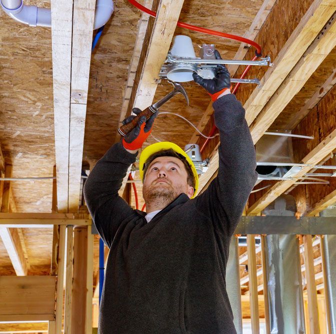 Construction worker installing electrical fixture in ceiling with hammer