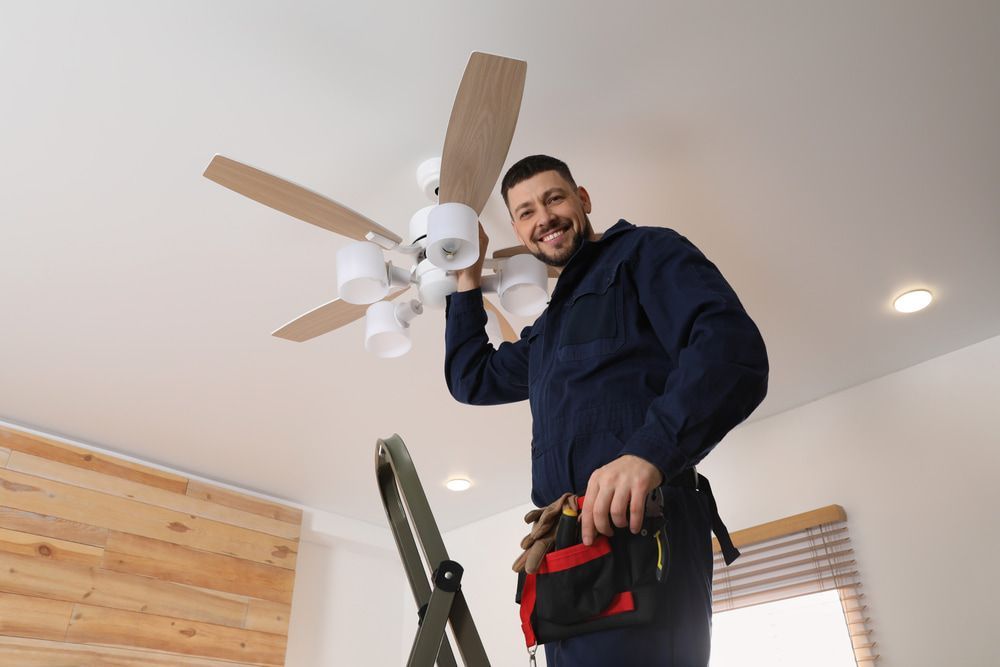 Person on a ladder installing a ceiling fan with lights; inside a room; smiling