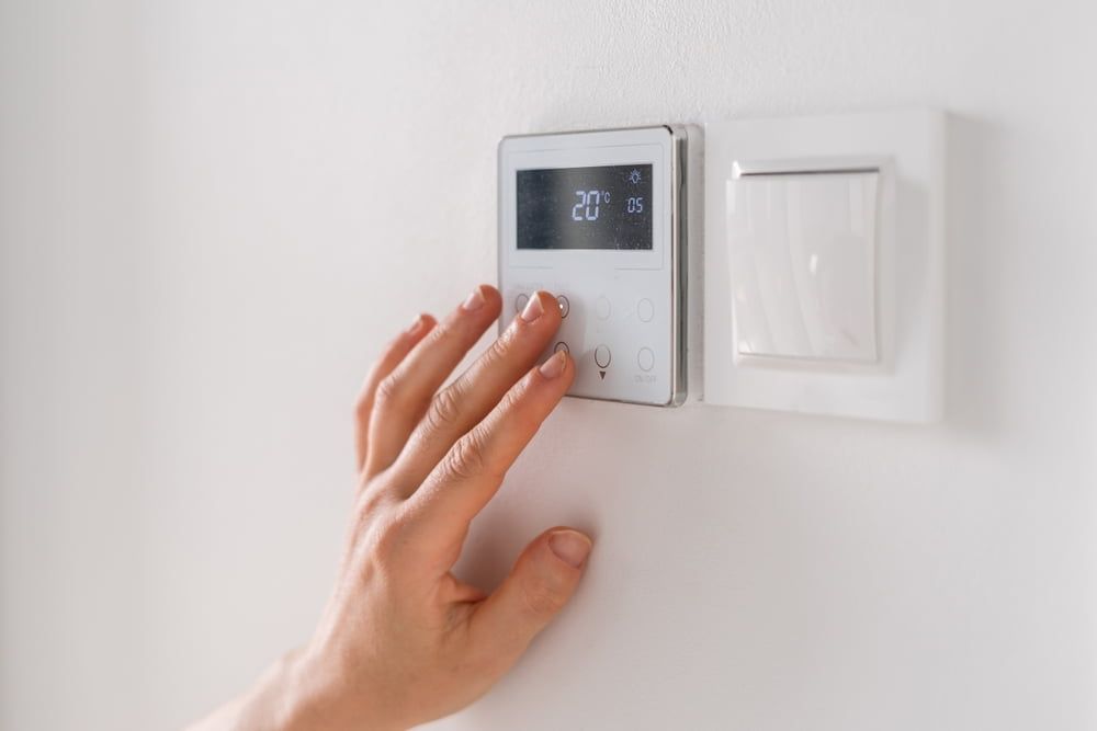 Hand adjusting a digital thermostat on a white wall