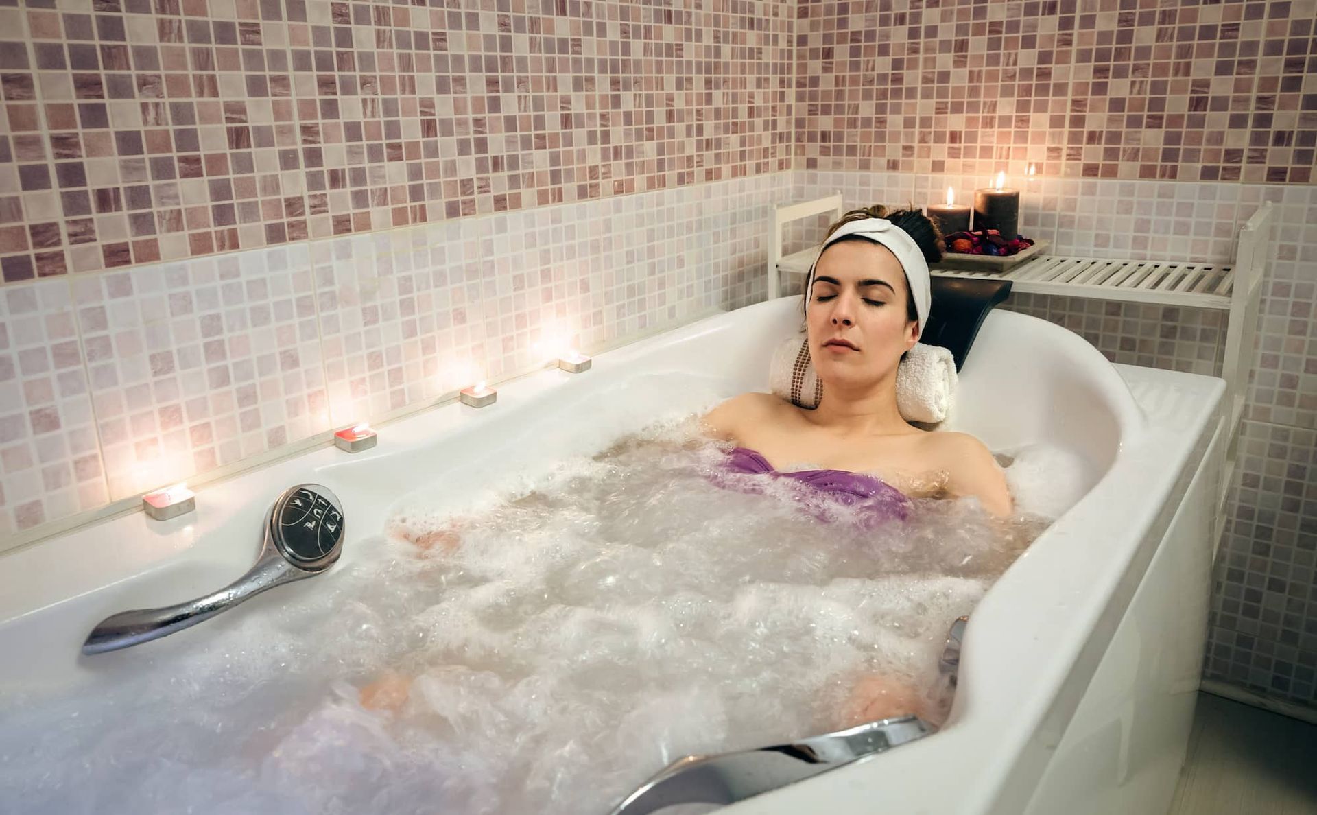 Woman relaxes in a bubble bath, lit by candles, in a spa setting
