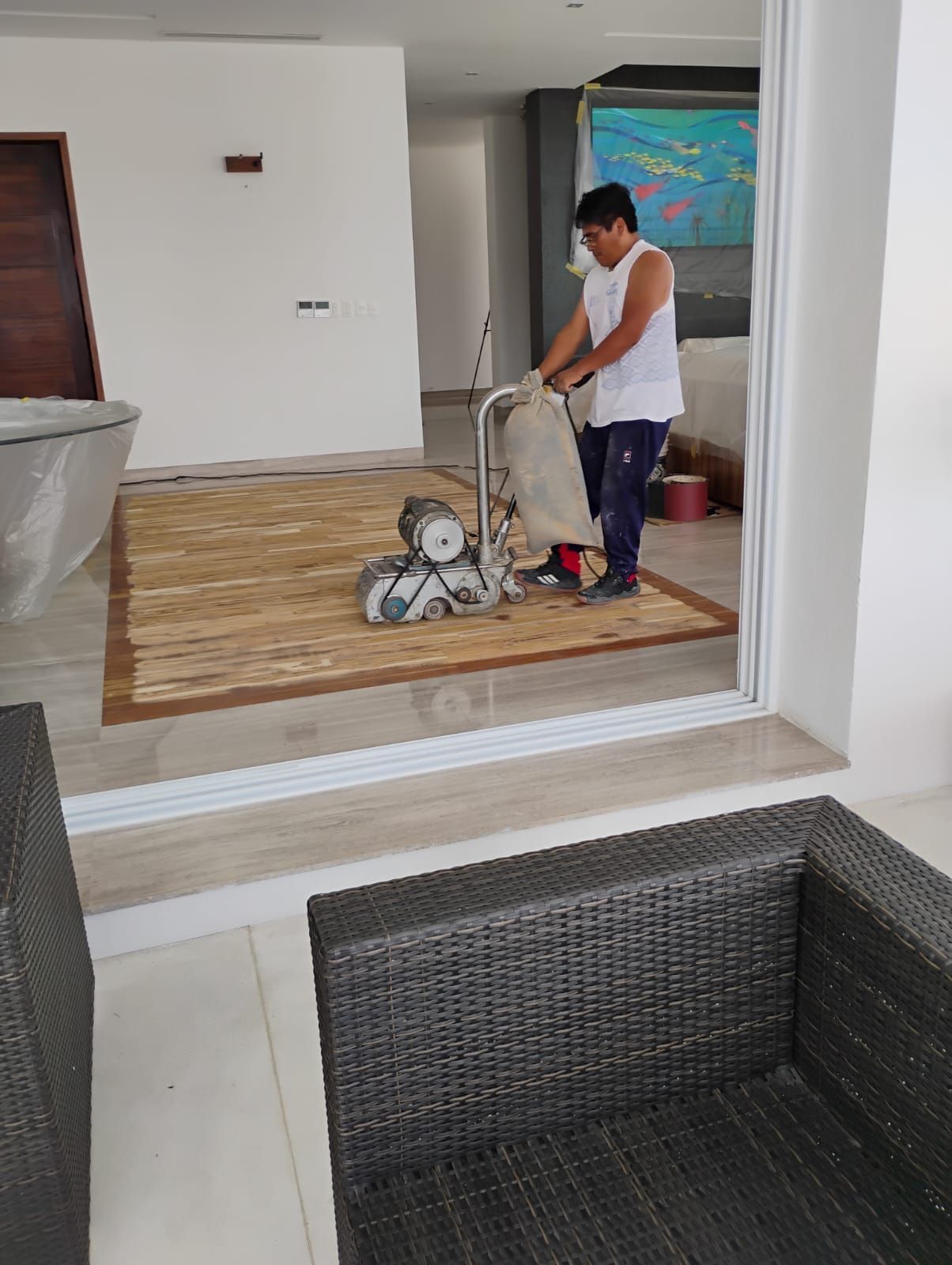 Un hombre está lijando un piso de madera con una máquina en una sala de estar.