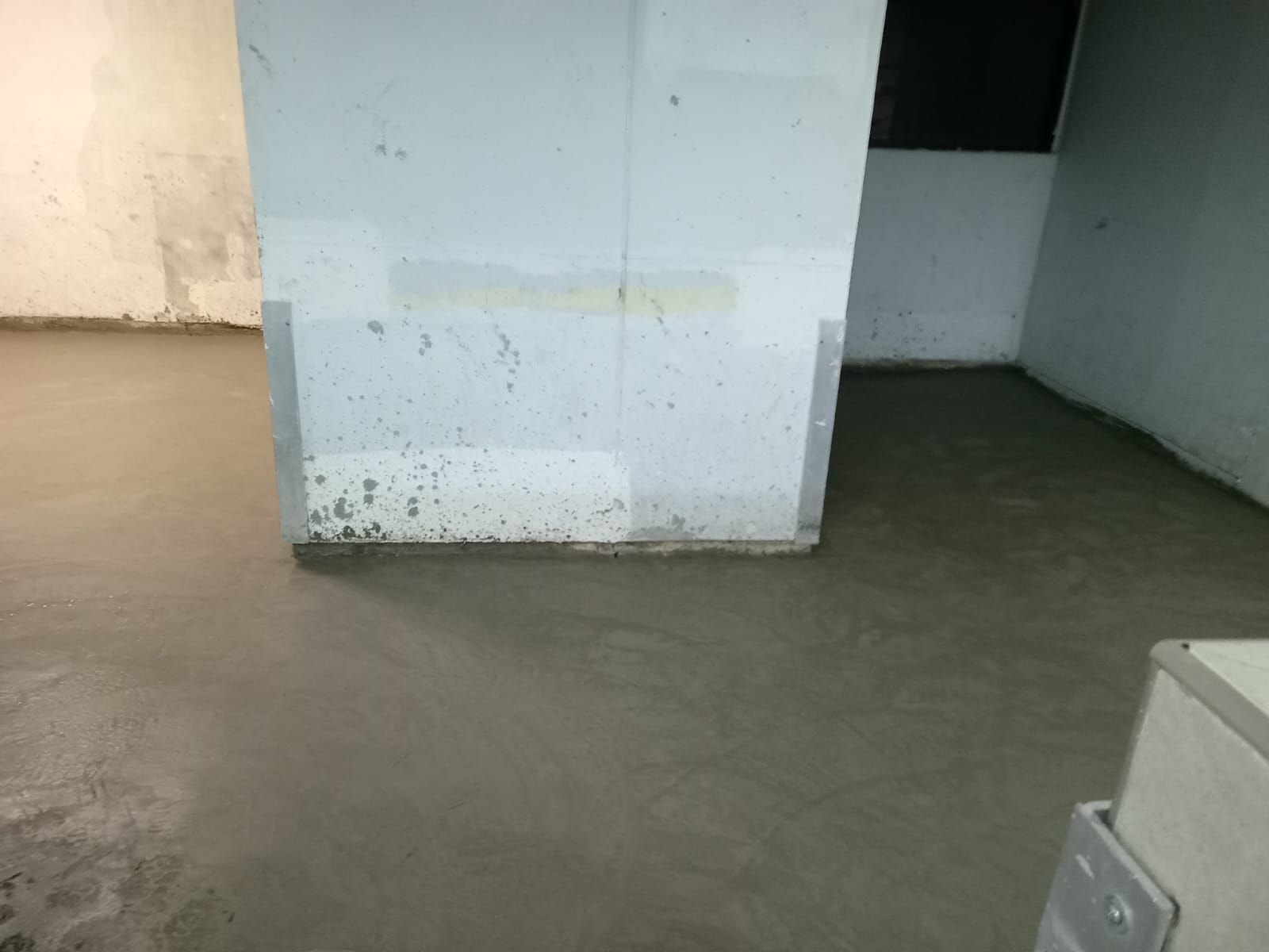 Una habitación con suelo de cemento y pared blanca.