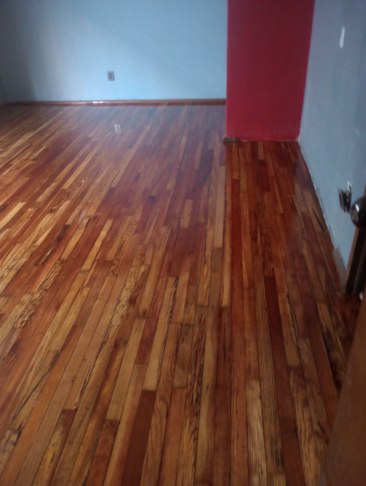 Una habitación con suelo de madera y una puerta roja.