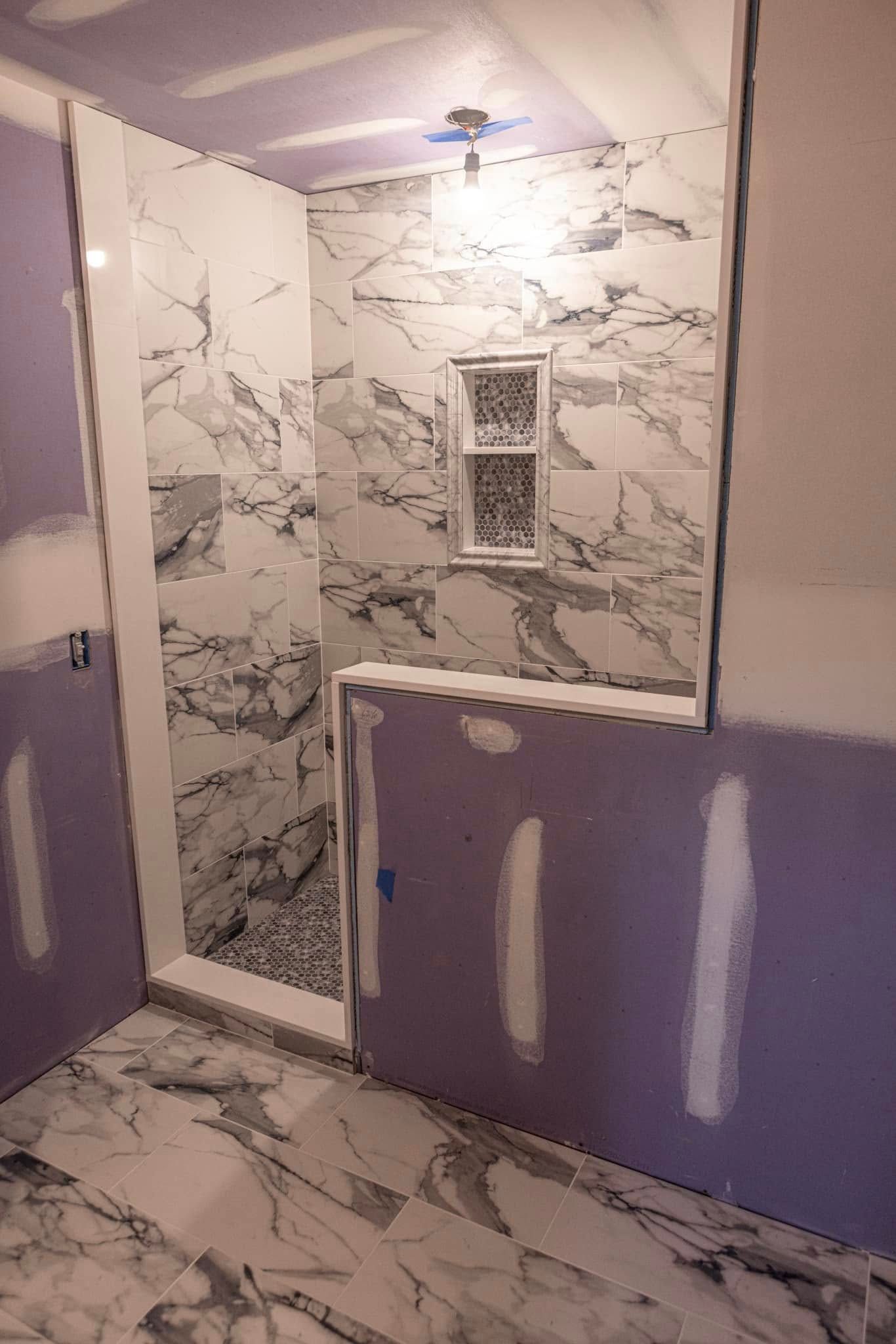 A bathroom under construction with marble tiles and a walk in shower.