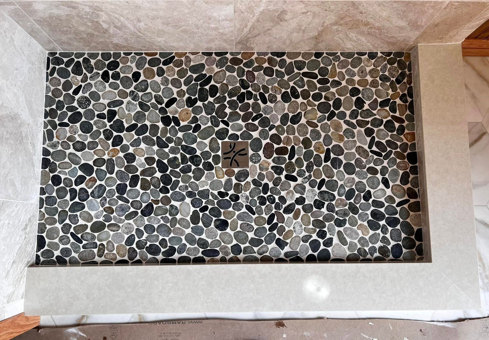 A shower stall with a tiled floor and a drain