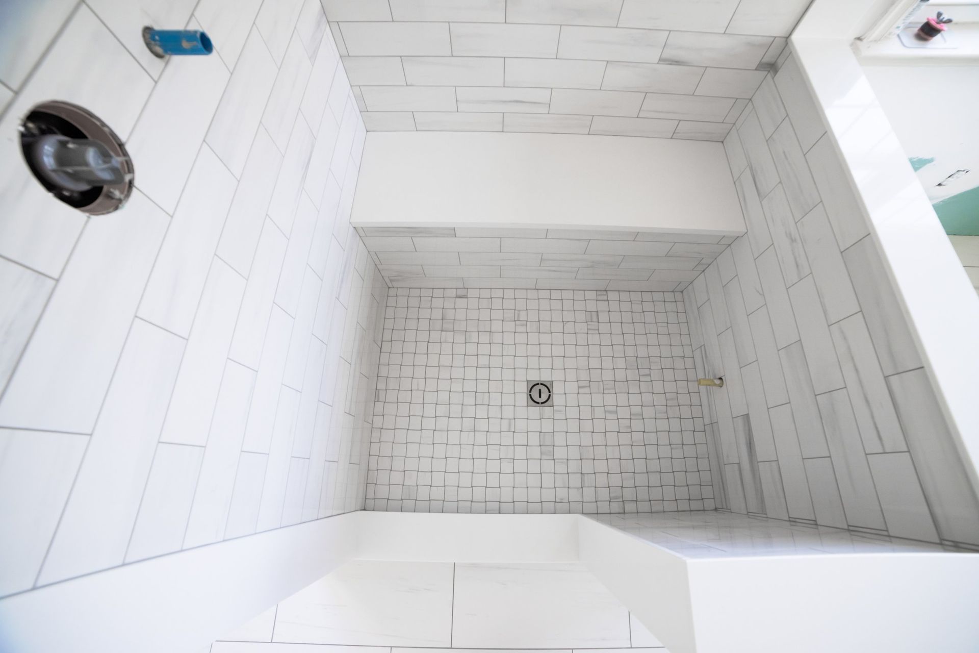 A bathroom with white tiles and a shower stall with a bench.