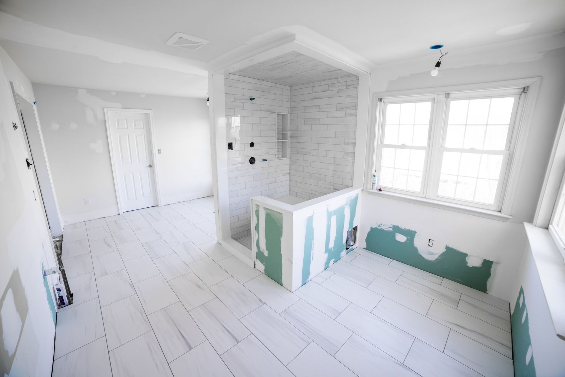 A bathroom under construction with white tiles and a walk in shower.