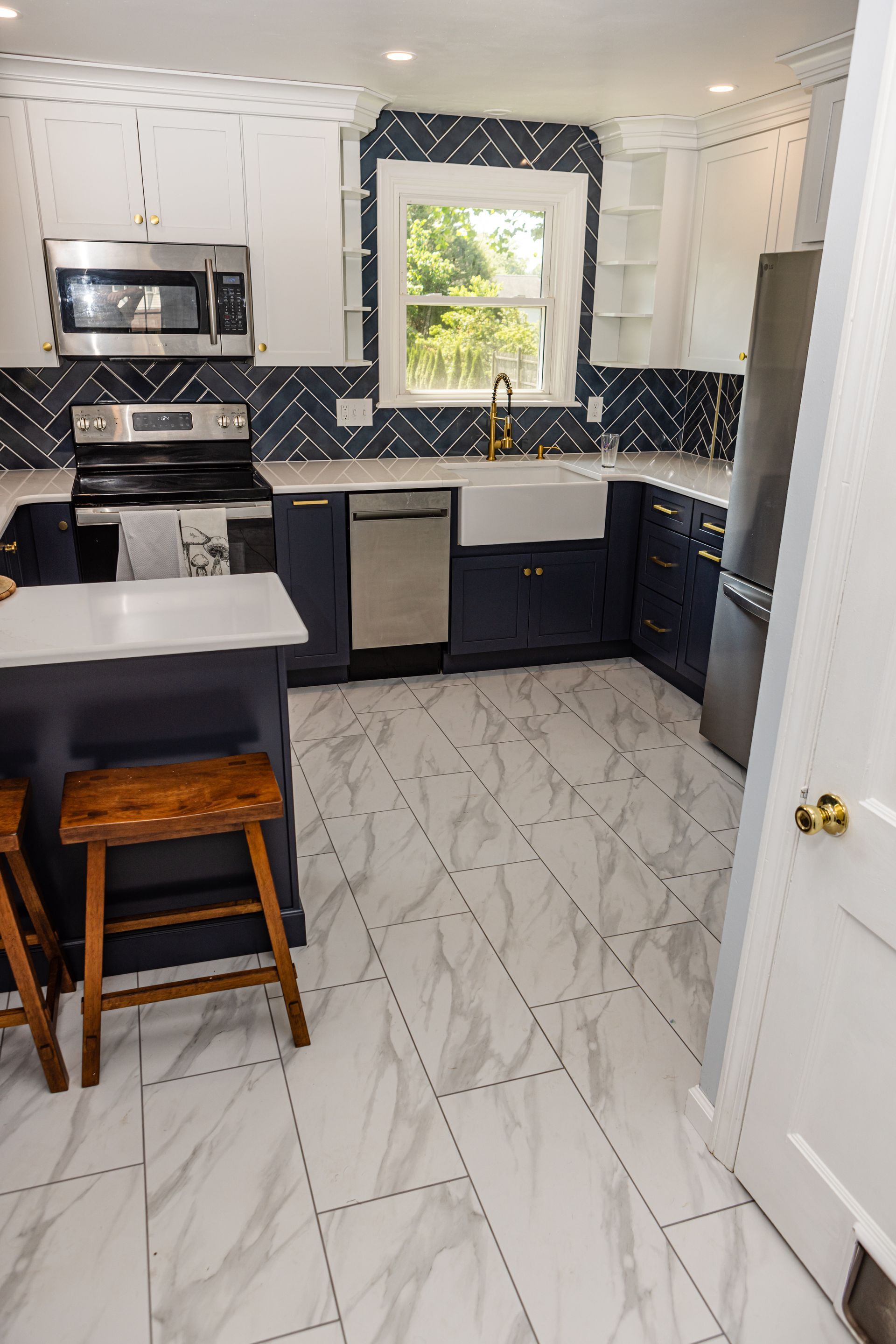 A kitchen with blue cabinets , white counter tops , stainless steel appliances , a sink , and a window.