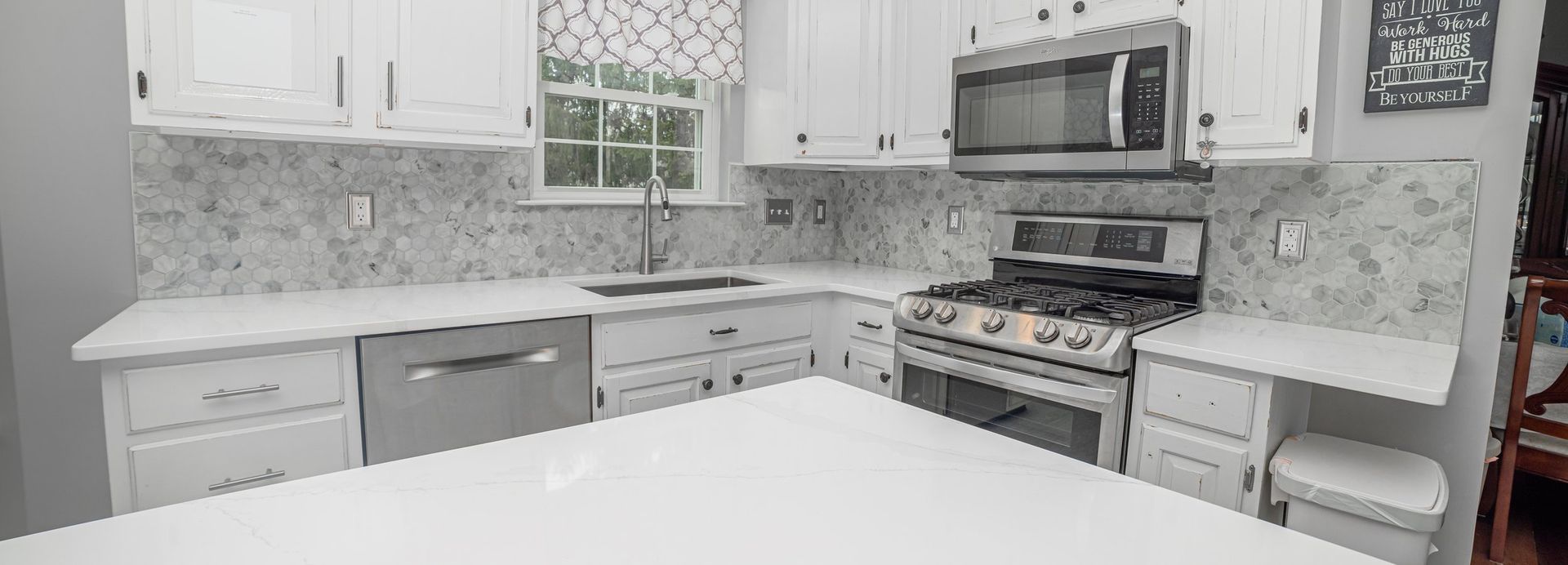 A kitchen with white cabinets , a stove , a microwave , and a sink.