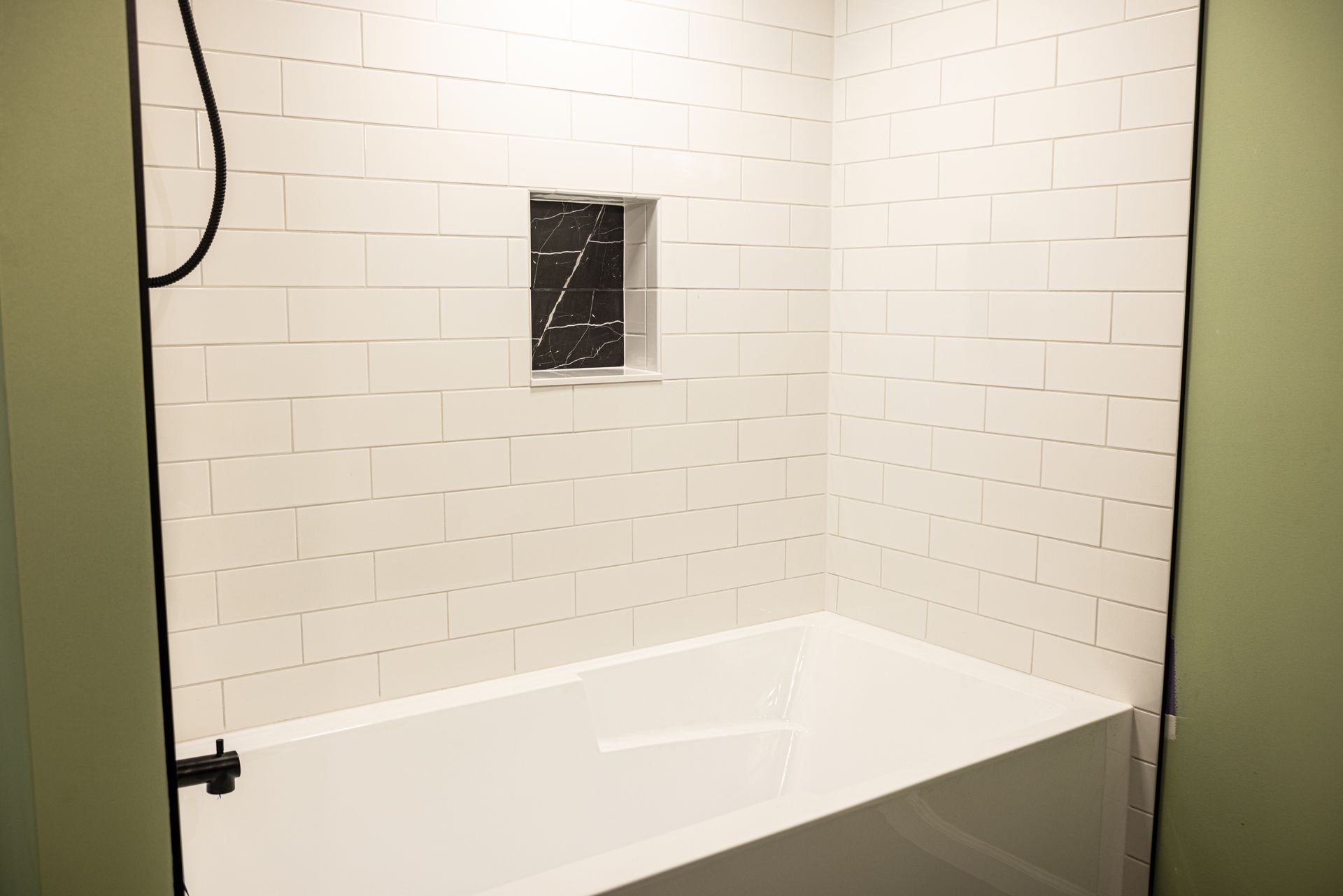 There is a bathtub in the bathroom with white tiles.