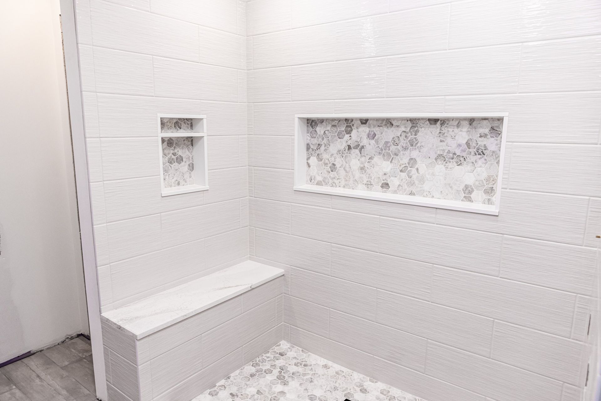 A bathroom with white tiles and a walk in shower with a bench.