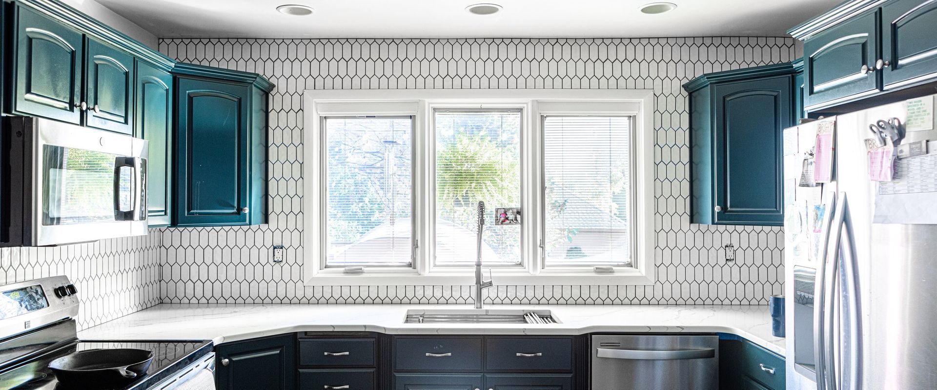 A kitchen with blue cabinets , stainless steel appliances , and a large window.