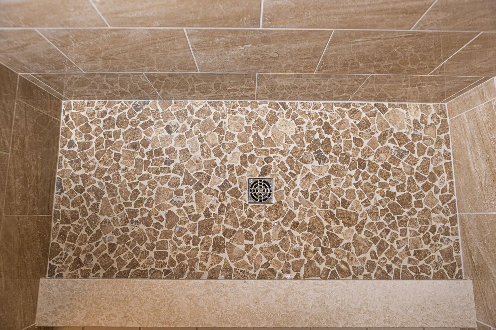 A walk in shower with a tiled floor and a drain.
