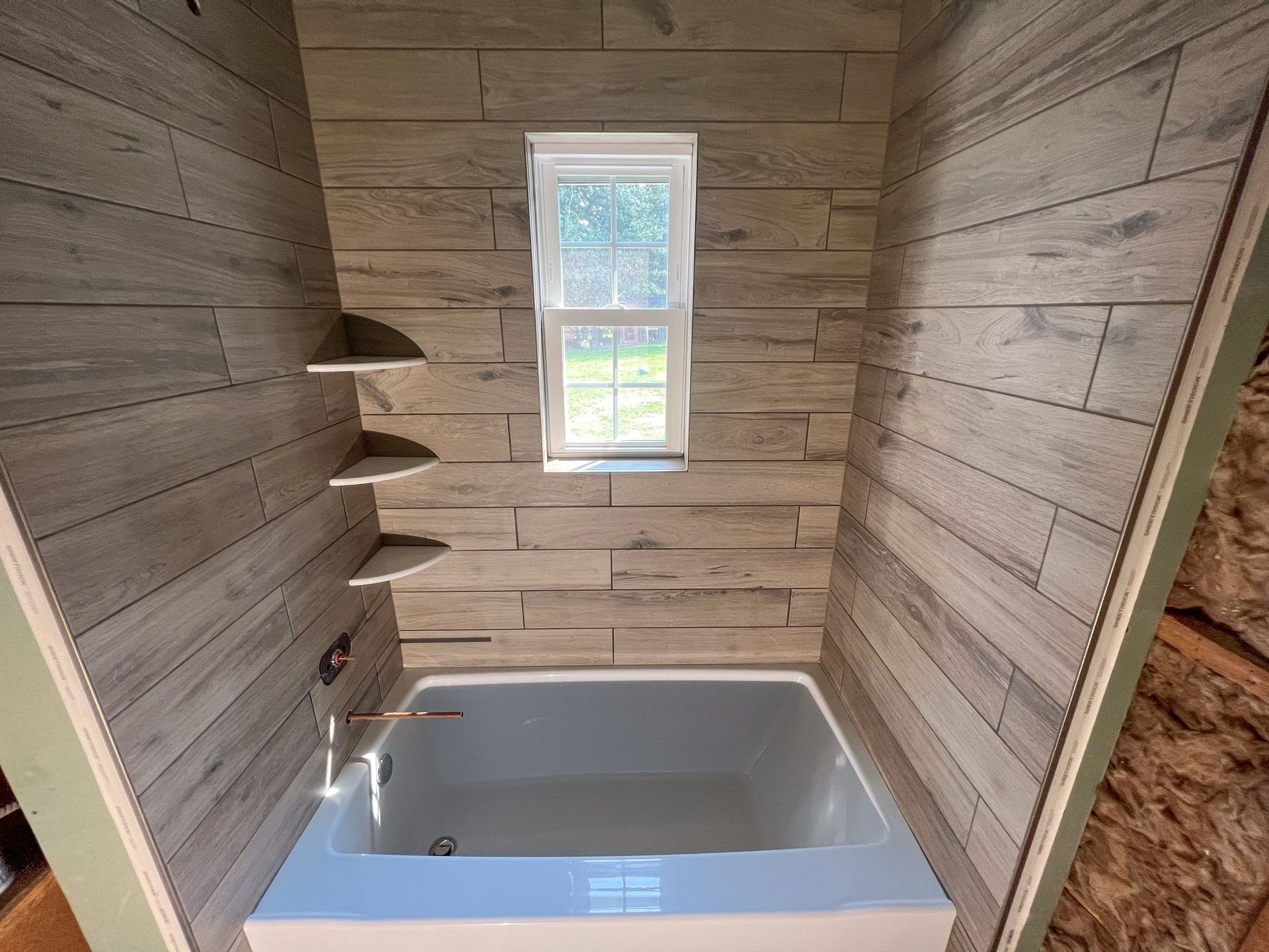 A bathtub in a bathroom with wooden walls and a window.