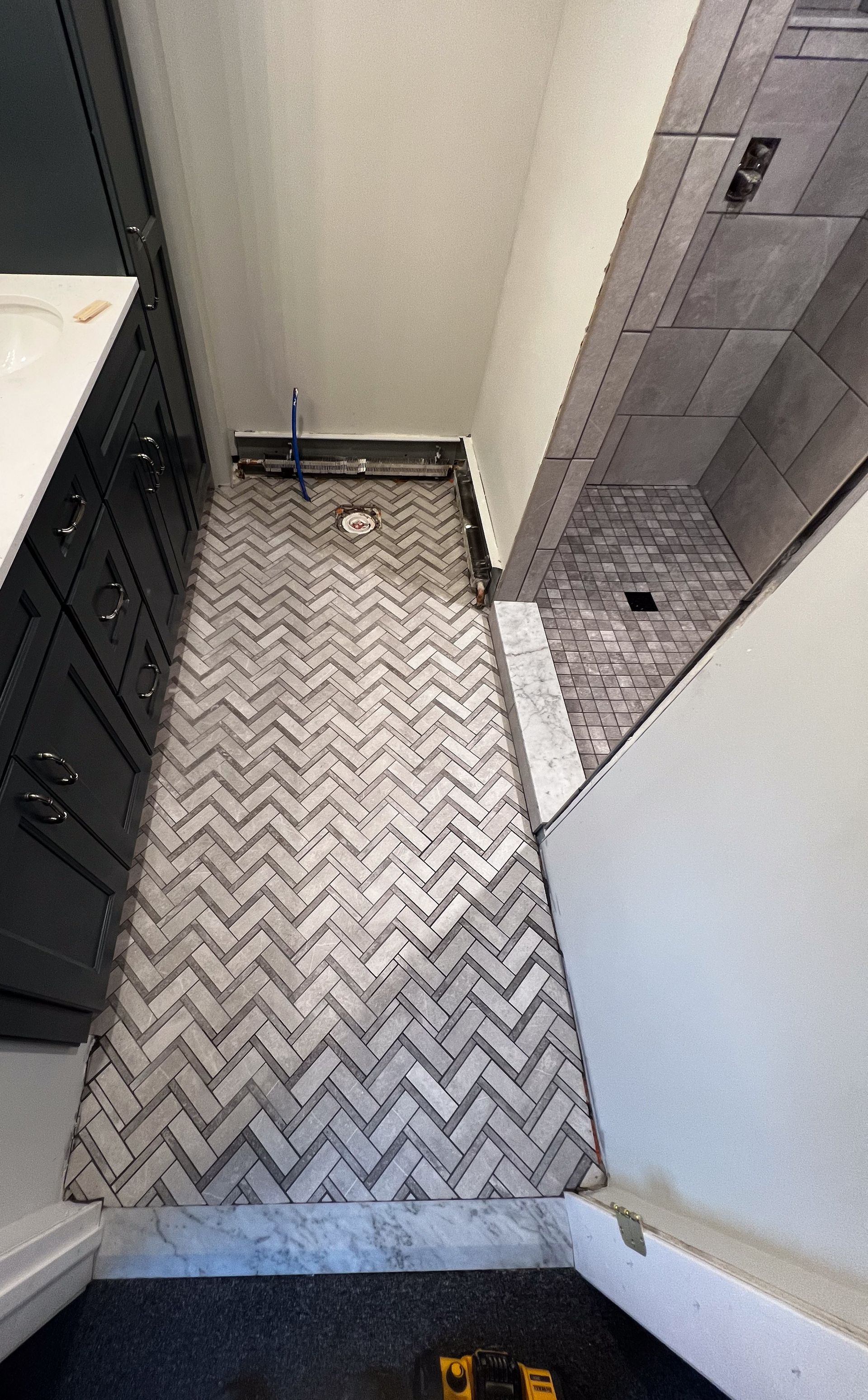 A bathroom with a herringbone tile floor and a walk in shower.