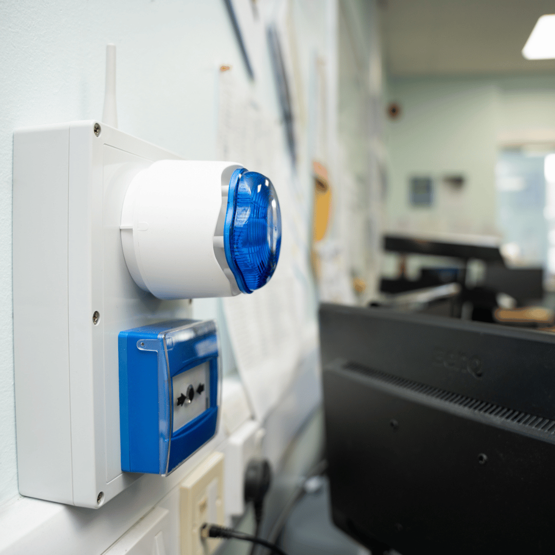 A blue and white alarm is mounted on a wall next to a computer monitor.