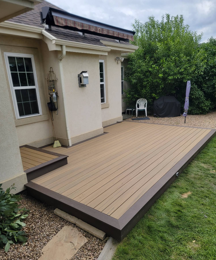 A tan, composite backyard deck with a dark brown border installed against the side of a house.