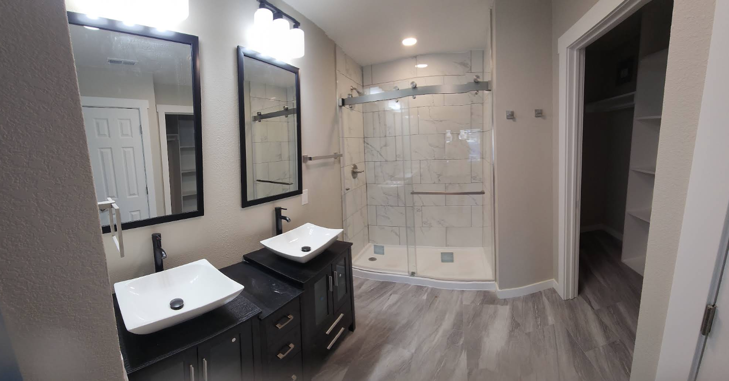 Modern bathroom featuring a double vanity with vessel sinks, two mirrors, a tiled glass shower, and a walk-in closet.