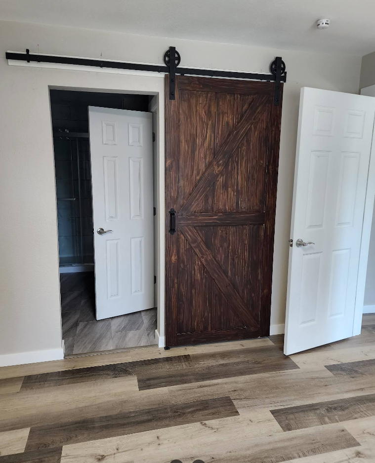 A dark wood sliding barn door sits between two white interior doors in a room with light wood-look vinyl flooring.