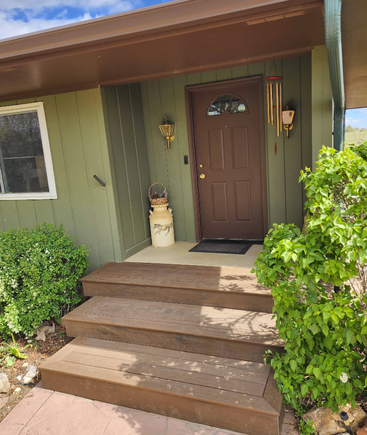 Exterior view of a home entrance with dark brown stairs leading up to a brown front door on a green wall.