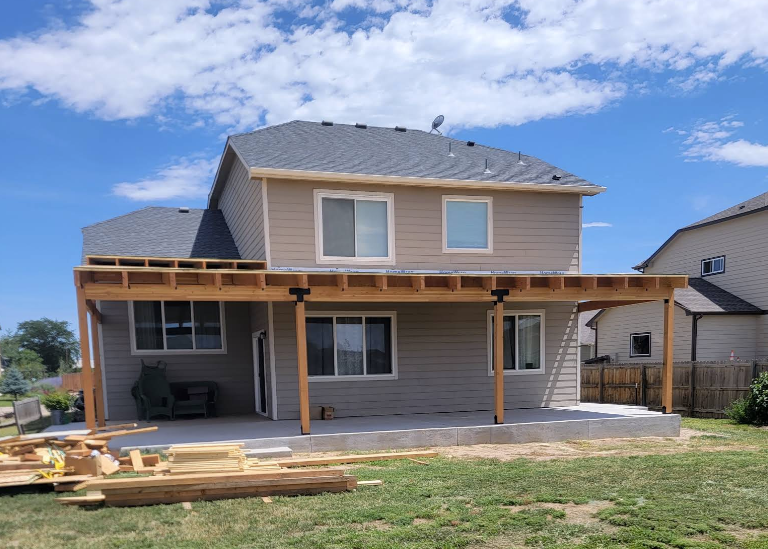The back of a tan two-story house featuring a newly constructed wooden patio cover over a concrete slab patio.
