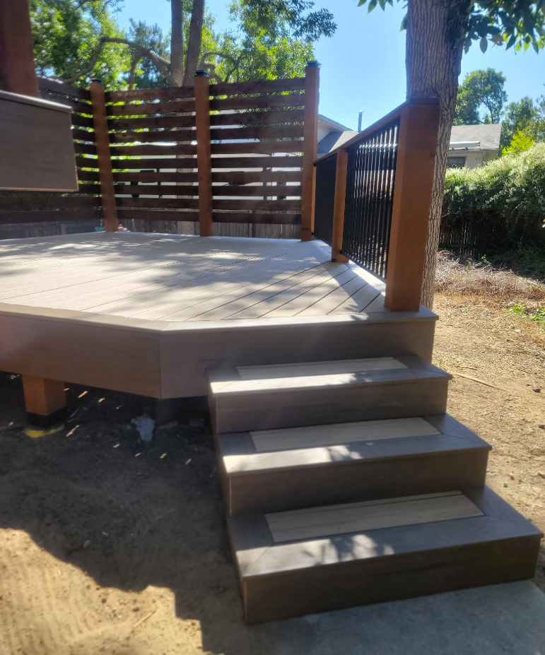 Brown composite steps lead up to a raised deck with horizontal wooden privacy fencing and a black metal railing.